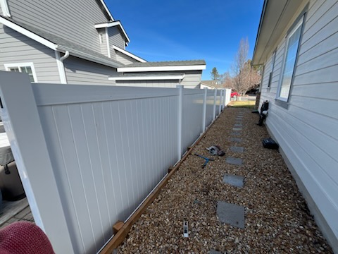 White vinyl privacy fence along a narrow gravel side yard in Prineville, Oregon