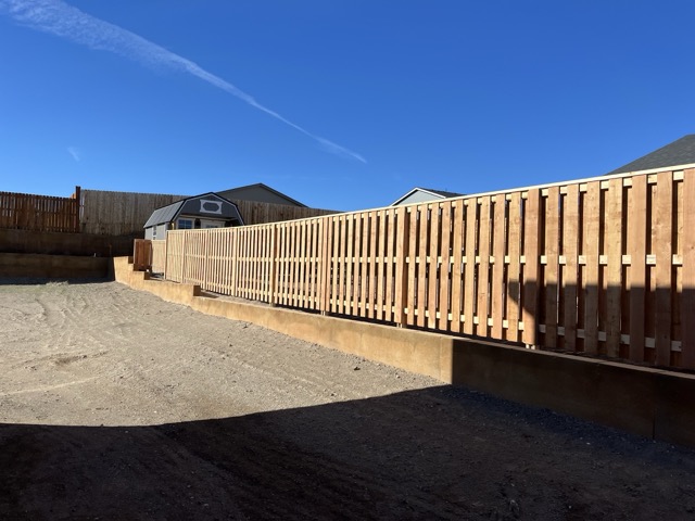 Newly built cedar privacy fence and retaining wall along a bare dirt yard after installation